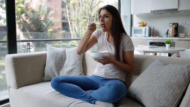 漂亮女人在家里一边看电视一边吃着一碗麦片视频素材