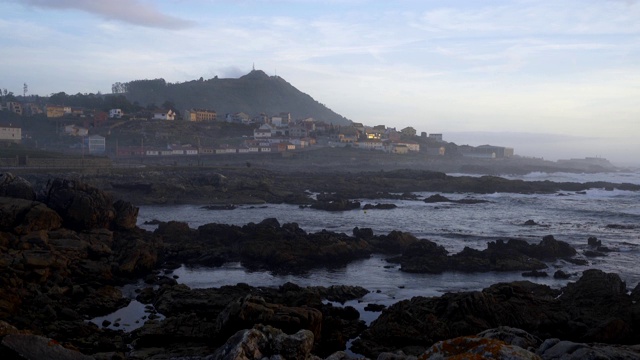 在西班牙，一个美丽的海岸景观岩石海滩与城市在日落的前景视频素材