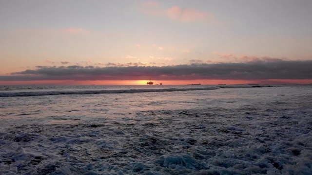 在洛杉矶亨廷顿海滩附近的南加州海岸的太平洋上，一个近海石油和天然气水力压裂钻井平台的日落镜头视频素材