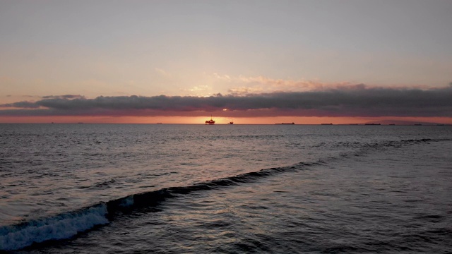 在洛杉矶亨廷顿海滩附近的南加州海岸的太平洋上，一个近海石油和天然气水力压裂钻井平台的日落镜头视频素材