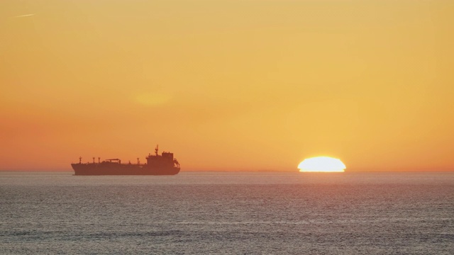 一艘货船在夕阳中航行在葡萄牙一个港口附近平静的海面上的美丽镜头。视频素材