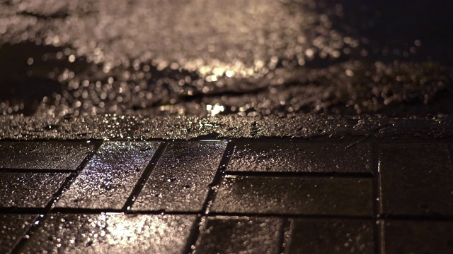 雨夜的城市街道，雨水在路灯下的人行道上流淌。视频素材