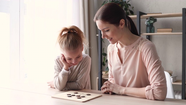 小女儿和年轻的妈妈在家里玩跳棋视频素材