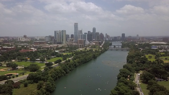 空中平移拍摄河中树木中的船在城市的天空，市中心的摩天大楼在阳光明媚的一天，而无人机从右到左飞行-奥斯汀，德克萨斯州视频素材