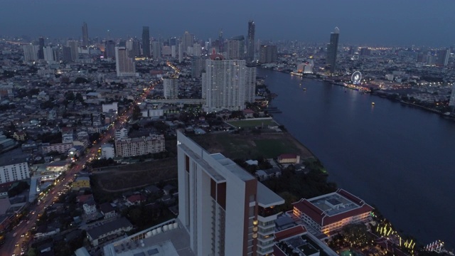 航拍的车辆在公路上的建筑物附近的河流在城市，无人机向前飞行的城市景观对天空在黄昏-曼谷，泰国视频素材