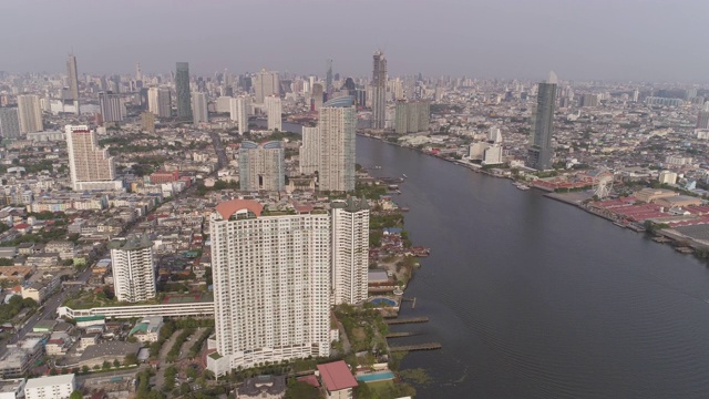 空中拍摄的河流在城市的建筑物对天空，无人机平移城市景观在晴朗的一天-曼谷，泰国视频素材