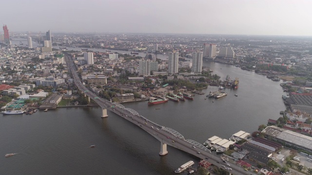 在阳光明媚的日子里，空中拍摄了河上桥梁上的车辆和城市里的船只，无人机向后飞过城市的天空-曼谷，泰国视频素材