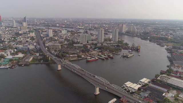 在阳光明媚的日子里，空中拍摄的车辆与船只在城市河上的桥梁上，无人机向前飞行的城市景观对天空-曼谷，泰国视频素材