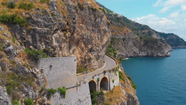 意大利南部山区蜿蜒公路的全景。海上陡峭的悬崖。危险的运动。一辆黑色轿车在柏油路上行驶。阳光明媚的夏天的一天。阿萨勒诺。本空间视频素材