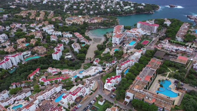 空中倾斜拍摄在城市建筑和度假村之间的海滩，无人机在多云的天空下向后飞行在靠近大海的建筑上——西班牙马略卡岛视频素材