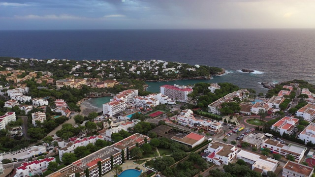 西班牙马略卡岛(Cales de Mallorca)，航拍多云天空下的城市建筑，无人机在向大海飞行的同时下降视频素材