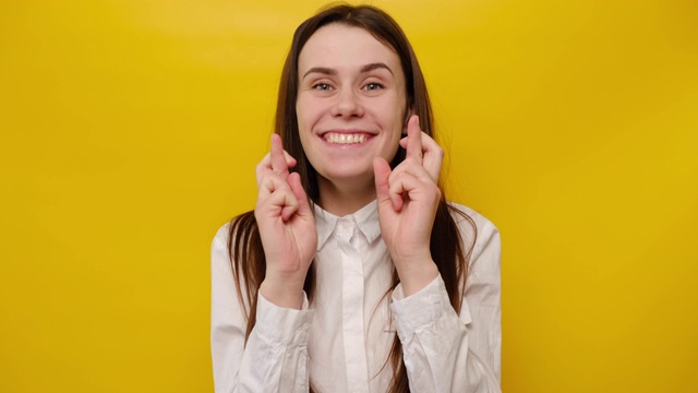 积极的年轻女子闭上眼睛保持手指交叉希望奇迹好结果，开朗的女孩真诚地乞求好运孤立在黄色工作室背景，乞求帮助的概念视频素材