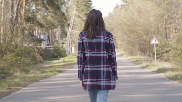 背影自信的白人黑发女人走在空旷的道路在阳光明媚的森林。千禧女游客享受户外一天。休闲，幸福，生活方式，休闲。视频素材