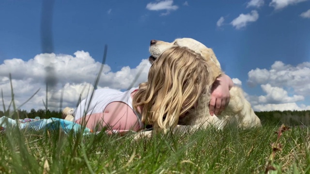 对宠物的爱。美丽的金毛猎犬带着一个女孩在阳光明媚的夏日的田野里休息，慢镜头视频素材