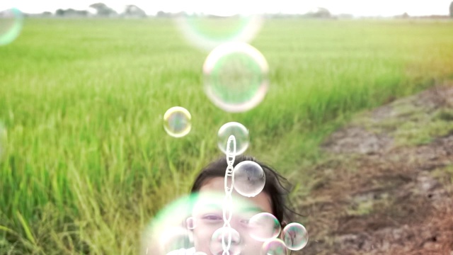 亚洲的孩子们笑着，在夏天的绿色稻田里吹泡泡，慢动作视频素材画面3