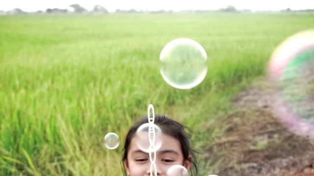 亚洲的孩子们笑着，在夏天的绿色稻田里吹泡泡，慢动作视频素材画面4