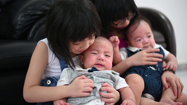 亚洲华人姐妹在客厅里照顾双胞胎弟弟视频素材