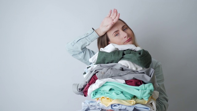 年轻的女人拿满干净的亚麻，家庭主妇洗完衣服后看起来很累，在家里工作视频素材