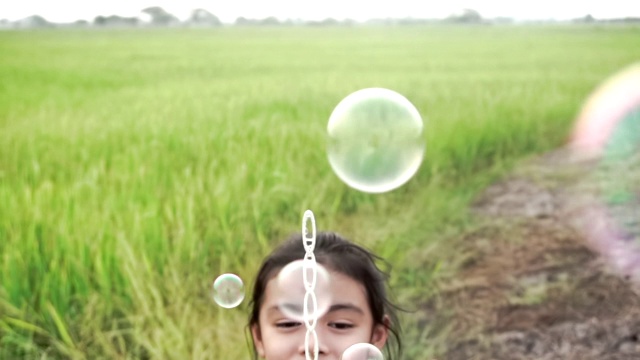亚洲的孩子们笑着，在一个夏天的绿色稻田吹泡泡，与慢动作股票视频有乐趣视频素材画面4
