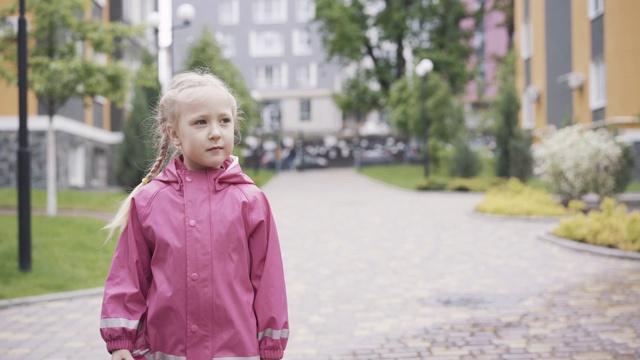 可爱的小女孩穿着防水服在户外的小巷里散步。漂亮的白人小孩穿着粉红色的衣服在雨天散步。童年,休闲的生活方式。视频素材