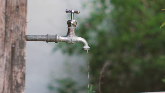 老旧生锈的老式金属水龙头漏水，一小股水流固定在建筑外墙的浅场深处视频素材