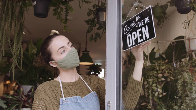 女小企业主、店主、商店老板在冠状病毒大流行期间戴着口罩，打开营业标牌视频素材