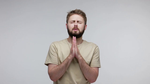 一名满脸胡须的不幸男子闭着眼睛绝望地祈祷着，抬起头向上帝祈祷，真诚地请求帮助视频素材