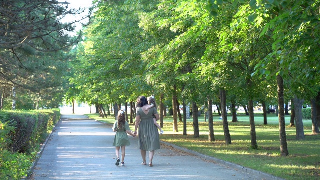 一位怀孕的母亲带着两个女儿走在绿色的公园里视频下载