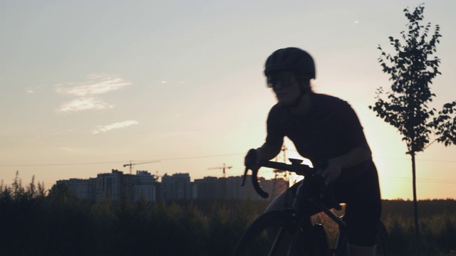 日落时分，一名女子打开自行车电脑，开始训练空中公路自行车。女性开始在阳光下骑自行车。努力锻炼。自行车和铁人三项训练。骑自行车的女人很开心视频素材