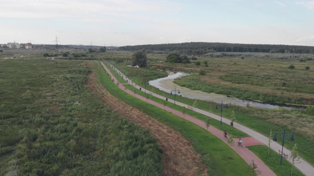 夏天，人们在热闹的步行街上骑自行车。游客在公园里骑自行车，无人机拍摄。在城市建筑的背景下，女性沿着河流骑车。自行车和铁人三项概念视频素材