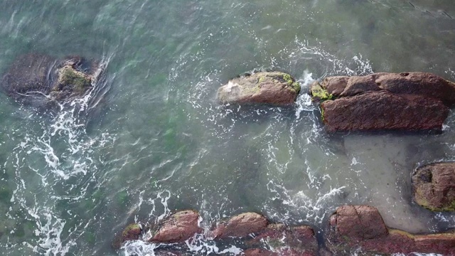 鸟瞰图的海浪打破在蓝色的海洋岩石。海浪对美丽的海滩鸟瞰图无人机4k拍摄。鸟瞰图的海浪撞击一个空的石头岩石悬崖从上面视频素材