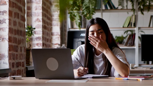 亚洲学生女孩打哈欠，睡着了，而看网络研讨会的笔记本电脑视频素材