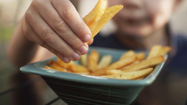 夏天，小男孩在咖啡馆里吃炸薯条视频素材