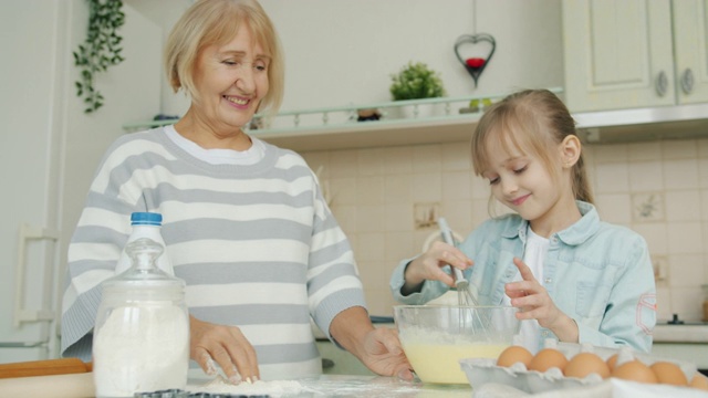 孩子和奶奶在做糕点和面，老太太加面粉跟孩子说话视频素材