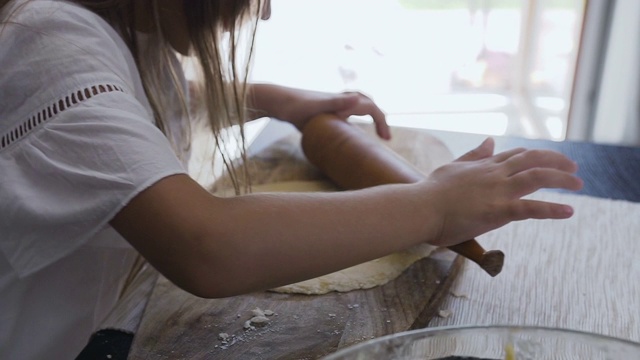 可爱的小女孩紧靠在铺满面粉的木桌上揉面团，用擀面杖在家里厨房里。在室内。女孩擀面团，烤饼干视频素材