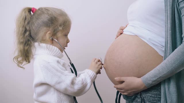 有趣的女孩用听诊器摸孕妇的肚子视频素材