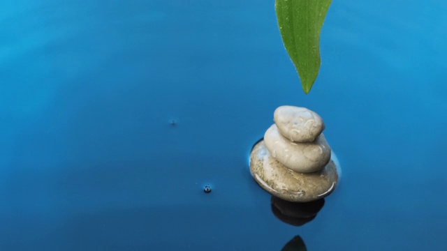 水滴落在金字塔上，绿叶落在蓝色的水中。水疗中心的背景。视频素材