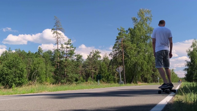 年轻的成年运动员在松树林中间的道路上玩滑板，慢镜头视频素材