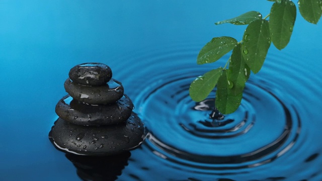 缓慢的运动。雨点落在蓝色的水中，背景是一堆石头和绿叶的树枝。视频素材