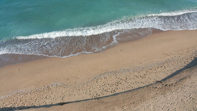 从上面看海岸线。航拍美丽的波涛汹涌的大海和泡沫的海浪。柔和的波浪在沙滩边拍打着并产生泡沫。鸟瞰画面。4K -超高清镜头视频素材