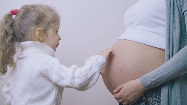 房间里穿着毛衣的女孩在怀孕妈妈的肚子上涂霜视频素材