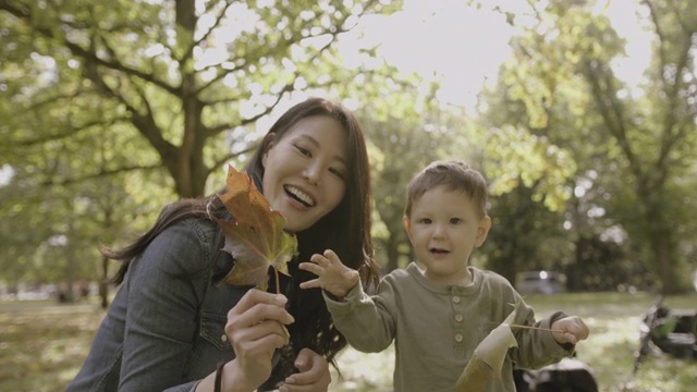 亚洲女性母亲与婴儿男孩儿子和秋天的树叶在公园里玩视频素材