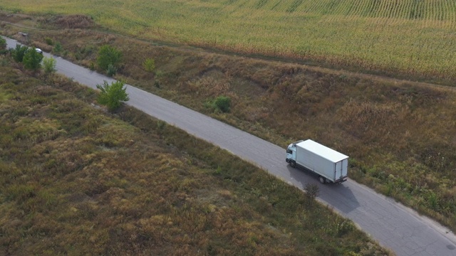 航拍的卡车与货物拖车驾驶在道路上运输货物。在乡村田野附近的高速公路上行驶的运货车。自然风景的观点。物流的概念。视频素材画面2