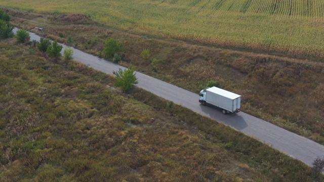 航拍的卡车与货物拖车驾驶在道路上运输货物。在乡村田野附近的高速公路上行驶的运货车。自然风景的观点。物流的概念。视频素材画面3