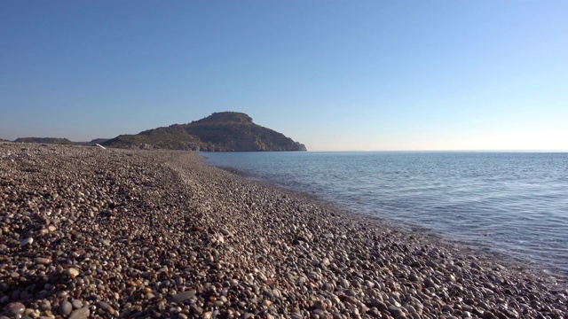 地中海沿岸，布满卵石的海滩，海浪，悬崖在背景中，希腊的罗德岛。视频素材