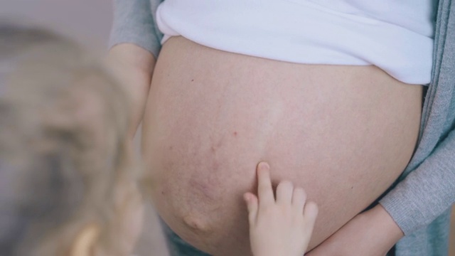 金发女孩在房间里给怀孕妈妈的肚子上涂霜视频素材