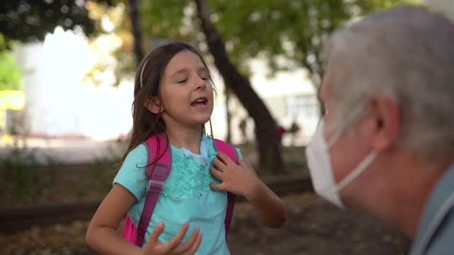 爷爷在学校院子里给孙女戴上防护口罩视频素材