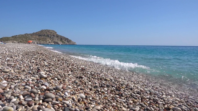 地中海沿岸，布满卵石的海滩，海浪，悬崖在背景中，希腊的罗德岛。视频素材