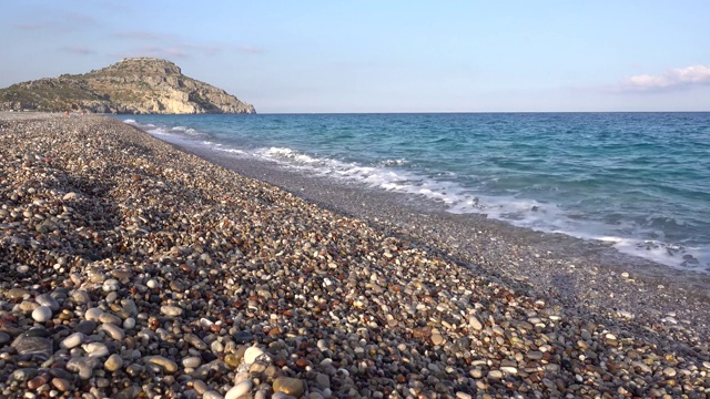 地中海沿岸，布满卵石的海滩，海浪，悬崖在背景中，希腊的罗德岛。视频素材