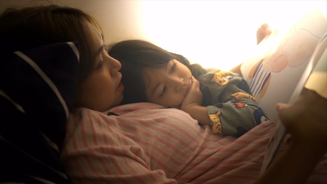 单身妈妈经常在女儿睡觉前给她讲故事。视频素材画面1